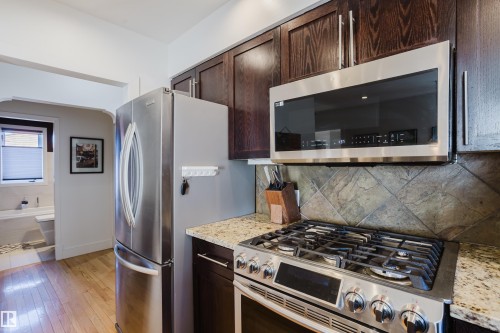 The kitchen features stainless steel appliances, including a gas range and microwave, set against granite countertops and dark wood cabinetry - 10643 66 Avenue, Edmonton, AB - Indoor Photo Showing Kitchen With Upgraded Kitchen