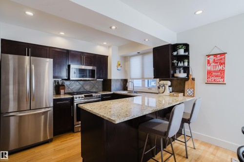 The kitchen features dark wood cabinetry, stainless steel appliances, and a U-shaped counter with a granite-style countertop - 10643 66 Avenue, Edmonton, AB - Indoor Photo Showing Kitchen