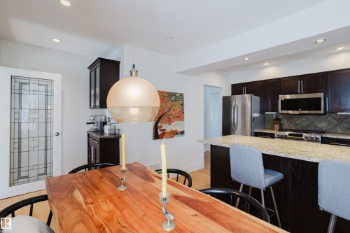 The kitchen features dark wood cabinetry, stainless steel appliances, and a light-colored granite countertop with a matching backsplash - 10643 66 Avenue, Edmonton, AB - Indoor Photo Showing Kitchen With Upgraded Kitchen