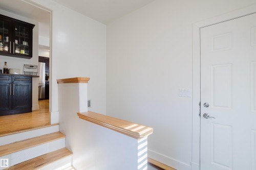 Entryway with white panel door, hardwood floors, and a partial wall with wood trim, leading to a kitchen with dark cabinetry - 10643 66 Avenue, Edmonton, AB - Indoor Photo Showing Other Room