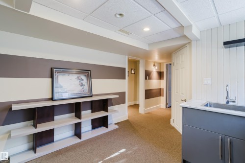 This room features a neutral carpeted floor, recessed lighting, and a utility sink with a stone countertop and dark cabinetry - 10643 66 Avenue, Edmonton, AB - Indoor Photo Showing Other Room