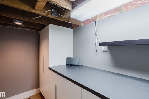 The property features a utility area with exposed ceiling joists, a built-in white storage cabinet, and a dark countertop with white lower cabinets - 10643 66 Avenue, Edmonton, AB - Indoor