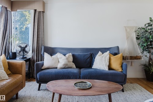 Living area featuring light-colored walls, hardwood flooring, and a large window with patterned drapes - 10643 66 Avenue, Edmonton, AB - Indoor Photo Showing Living Room