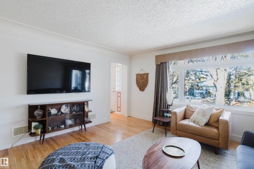 Bright living area featuring hardwood floors and a large window providing natural light and exterior views - 10643 66 Avenue, Edmonton, AB - Indoor Photo Showing Living Room