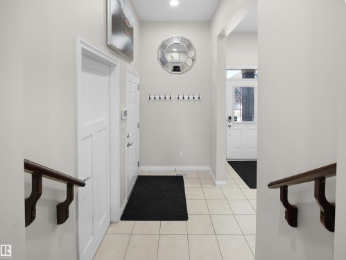 Inviting entryway featuring light-colored tile flooring, a white front door with a window, and a dark wood handrail - 4405 Crabapple Landing Landing, Edmonton, AB - Indoor Photo Showing Other Room