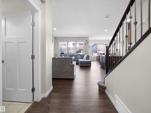The property features a spacious living area with large windows, dark wood-style flooring, and a staircase with an ornamental railing - 4405 Crabapple Landing Landing, Edmonton, AB - Indoor Photo Showing Other Room