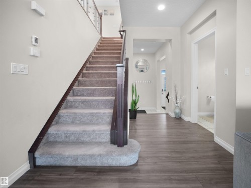 The property features a staircase with carpeted treads and a dark wood handrail, complemented by dark wood-style flooring in the entryway - 4405 Crabapple Landing Landing, Edmonton, AB - Indoor Photo Showing Other Room