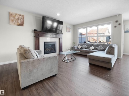 Living area featuring rich dark wood flooring, a fireplace with a dark wood mantel and white tile surround, and large windows providing natural illumination - 4405 Crabapple Landing Landing, Edmonton, AB - Indoor Photo Showing Living Room With Fireplace