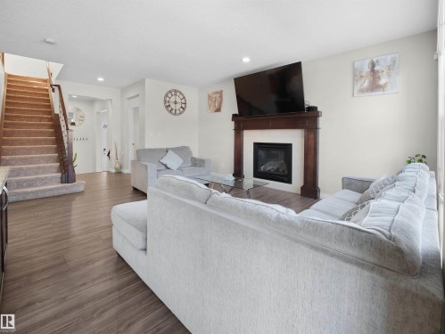 The living area features wood-look flooring, a fireplace with a dark wood mantle, and a carpeted staircase with a wood handrail - 4405 Crabapple Landing Landing, Edmonton, AB - Indoor Photo Showing Living Room With Fireplace
