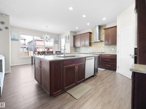 The kitchen features a large island with a sink and granite countertops, complemented by dark wood cabinetry and stainless steel appliances - 4405 Crabapple Landing Landing, Edmonton, AB - Indoor Photo Showing Kitchen