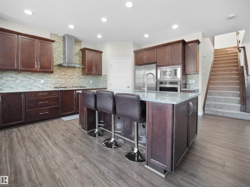 The kitchen features dark wood cabinetry, stainless steel appliances, a center island with a light-colored countertop, and recessed lighting - 4405 Crabapple Landing Landing, Edmonton, AB - Indoor Photo Showing Kitchen With Upgraded Kitchen