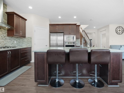 The kitchen features rich wood cabinetry, stainless steel appliances, a light-colored countertop, and a tiled backsplash - 4405 Crabapple Landing Landing, Edmonton, AB - Indoor Photo Showing Kitchen With Double Sink