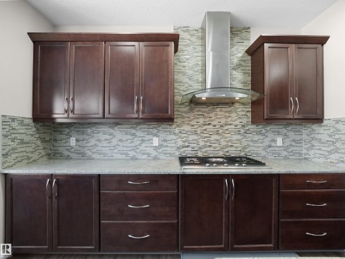 The kitchen features dark wood cabinetry, a mosaic tile backsplash, a stainless steel range hood, and a built-in gas cooktop - 4405 Crabapple Landing Landing, Edmonton, AB - Indoor Photo Showing Kitchen
