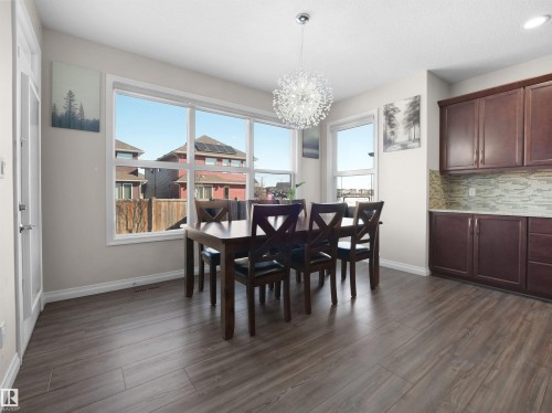 This dining area features wood-look flooring, large windows providing natural light, and a modern chandelier - 4405 Crabapple Landing Landing, Edmonton, AB - Indoor Photo Showing Dining Room