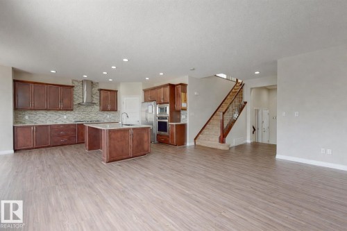 This expansive living area features wide plank flooring and recessed lighting, leading to a kitchen with wood cabinetry, stainless steel appliances, and an island with a sink - 4405 Crabapple Landing Landing, Edmonton, AB - Indoor Photo Showing Kitchen