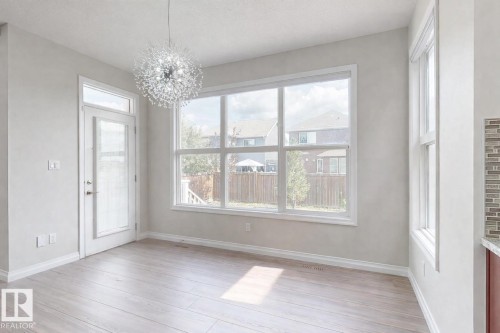 This bright room features light-colored flooring, a modern chandelier, and large windows, including a glass-paneled door - 4405 Crabapple Landing Landing, Edmonton, AB - Indoor Photo Showing Other Room