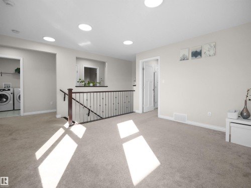 Spacious carpeted landing area with a dark wood and metal stair railing, and a laundry area visible through an open doorway - 4405 Crabapple Landing Landing, Edmonton, AB - Indoor