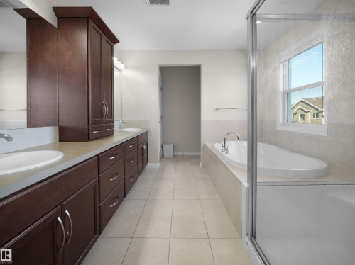 Well-appointed bathroom featuring a double vanity with dark wood cabinetry, a built-in soaking tub, and a window providing natural light - 4405 Crabapple Landing Landing, Edmonton, AB - Indoor Photo Showing Bathroom