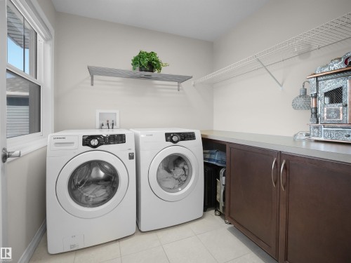 The laundry room features two front-loading machines, ample counter space, and integrated cabinetry with silver handles - 4405 Crabapple Landing Landing, Edmonton, AB - Indoor Photo Showing Laundry Room