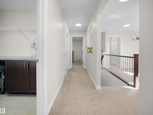 A bright hallway featuring neutral carpeting, recessed lighting, and a dark wood and metal stair railing - 4405 Crabapple Landing Landing, Edmonton, AB - Indoor Photo Showing Other Room