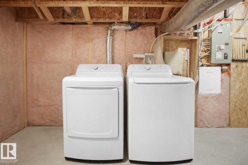 The utility area features a white top-loading washing machine and a white front-loading dryer, with exposed wooden beams and insulation visible - 4405 Crabapple Landing Landing, Edmonton, AB - Indoor Photo Showing Laundry Room