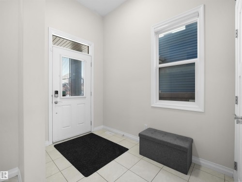 The property features a front entry with a white door, an overhead transom window, and a vertical window providing natural light - 4405 Crabapple Landing Landing, Edmonton, AB - Indoor Photo Showing Other Room