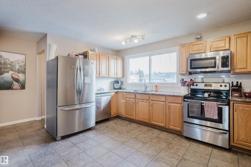 The kitchen features stainless steel appliances, light wood cabinetry, a tiled backsplash, and tiled flooring - 8707 151 Avenue, Edmonton, AB - Indoor Photo Showing Kitchen