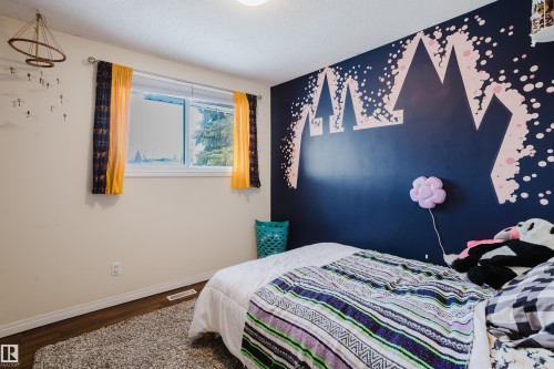 This room features a window providing natural light, warm-toned walls, and dark flooring - 8707 151 Avenue, Edmonton, AB - Indoor Photo Showing Bedroom