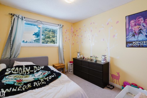 This room features light yellow walls, a window with a view of greenery, and light-colored carpeting - 8707 151 Avenue, Edmonton, AB - Indoor Photo Showing Bedroom