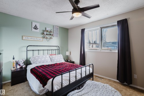 This room features a window with dark curtains, a ceiling fan with integrated lighting, and light-colored walls - 8707 151 Avenue, Edmonton, AB - Indoor Photo Showing Bedroom