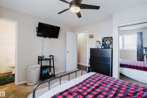 This room features a ceiling fan with integrated lighting, a mirrored closet door, and a door leading to a bathroom with a toilet - 8707 151 Avenue, Edmonton, AB - Indoor Photo Showing Bedroom