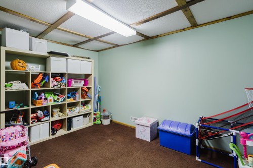This room features a light-colored wall, a textured ceiling with exposed wooden beams, and soft brown carpeting - 8707 151 Avenue, Edmonton, AB - Indoor