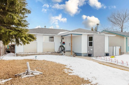 The property features a white exterior with grey shingle accents and a dark roof, complemented by a front yard with a partial lawn and a paved driveway - 8707 151 Avenue, Edmonton, AB - Outdoor