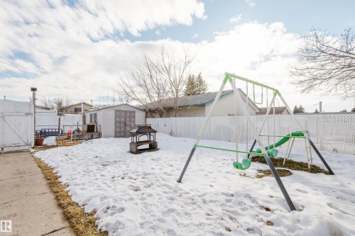 The property features a spacious yard with a white fence, a storage shed, and a swing set - 8707 151 Avenue, Edmonton, AB - Outdoor