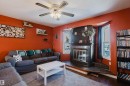 Living area featuring a ceiling fan with integrated lighting, a corner fireplace with a black tile hearth, and hardwood flooring - 8707 151 Avenue, Edmonton, AB  - Indoor Photo Showing Living Room With Fireplace 