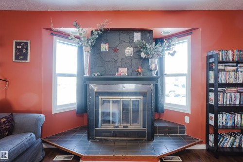 Living space featuring a central fireplace with a dark tile hearth and surround, framed by two windows providing natural light - 8707 151 Avenue, Edmonton, AB - Indoor With Fireplace