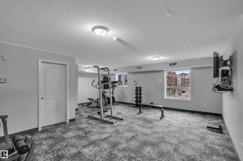The property features a well-equipped fitness area with various exercise machines, free weights, and a wall-mounted television - 320 392 Silver Berry Road, Edmonton, AB - Indoor Photo Showing Gym Room