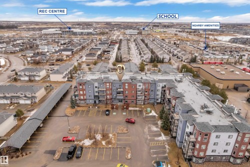 Aerial view of the property with a visible parking lot, covered parking structure, and surrounding neighborhood - 320 392 Silver Berry Road, Edmonton, AB - Outdoor With View