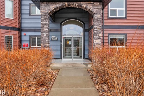 The property features a welcoming arched entrance with stone accents, glass double doors, and a concrete pathway leading to the entrance - 320 392 Silver Berry Road, Edmonton, AB - Outdoor With Fireplace