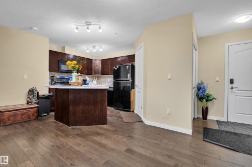 The property features hardwood floors, a kitchen with dark cabinetry, a kitchen island with a light-colored countertop, and a white entry door - 320 392 Silver Berry Road, Edmonton, AB - Indoor Photo Showing Kitchen