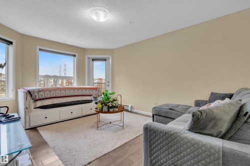 The living area features light-colored walls, hardwood flooring, and a large window providing views of the distant buildings and landscape - 320 392 Silver Berry Road, Edmonton, AB - Indoor