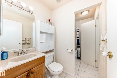 The bathroom features a vanity with a light wood cabinet and a single sink, an overhead light fixture, and a toilet with an integrated storage unit - 11415 32 Avenue, Edmonton, AB - Indoor Photo Showing Bathroom