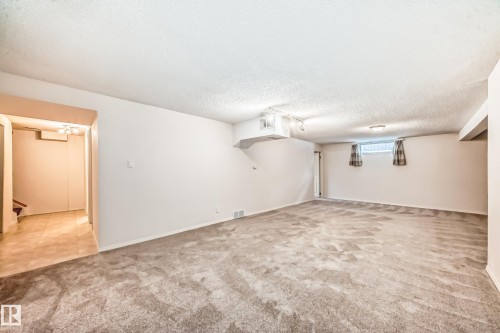 This expansive room features light-colored walls and grey carpet, with additional tiled flooring visible through an open doorway - 11415 32 Avenue, Edmonton, AB - Indoor