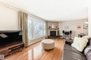 This living area features hardwood floors, a prominent brick fireplace with a mantle, and large windows that provide natural light - 11415 32 Avenue, Edmonton, AB  - Indoor Photo Showing Living Room With Fireplace 