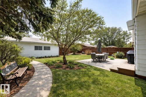 The property features a well-maintained lawn, mature trees, a concrete pathway, and a patio with outdoor seating - 11415 32 Avenue, Edmonton, AB - Outdoor