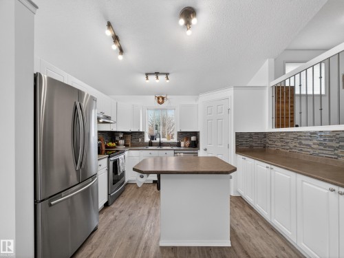 The kitchen features stainless steel appliances, white cabinetry, a central island with a countertop, and wood-look flooring - 1665 Tompkins Place, Edmonton, AB - Indoor Photo Showing Kitchen With Stainless Steel Kitchen With Double Sink