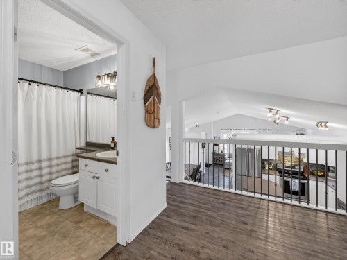 The property features a bathroom with a white vanity and a white shower curtain, visible from a hallway with dark wood-style flooring - 1665 Tompkins Place, Edmonton, AB - Indoor