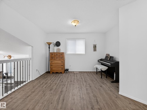 Versatile open area featuring hardwood flooring, a white railing with black spindles, and a window with blinds providing natural light - 1665 Tompkins Place, Edmonton, AB - Indoor