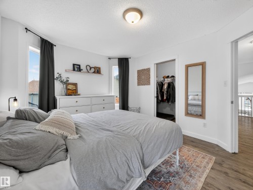 The bedroom features hardwood style flooring, a ceiling-mounted light fixture, and two windows with dark curtains - 1665 Tompkins Place, Edmonton, AB - Indoor Photo Showing Bedroom