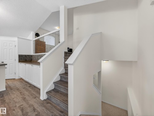 The property features stairs with wooden treads and white risers, a white railing with dark vertical balusters, and wood-look flooring on the lower level - 1665 Tompkins Place, Edmonton, AB - Indoor Photo Showing Other Room